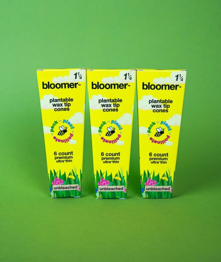 Three packs of Bloomer 1 1/4 inch cones displayed on a vibrant green background, showcasing eco-friendly smoking solutions for pollinator conservation.