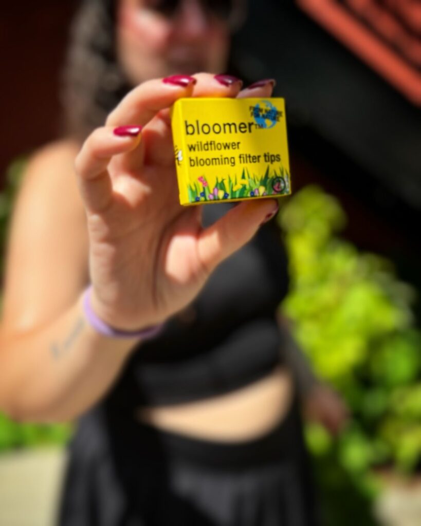 A person holding a Bloomer Tips box, showcasing eco-friendly smoking accessories designed to support pollinator health