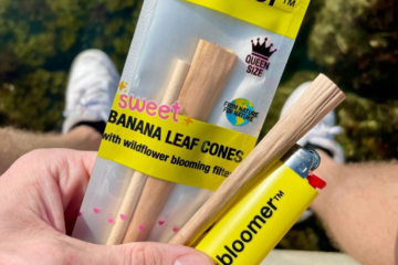 Man holding Sweet Banana Leaf Cone with Bloomer Lighter. Sitting on top of a tall building with an arial forest background view.